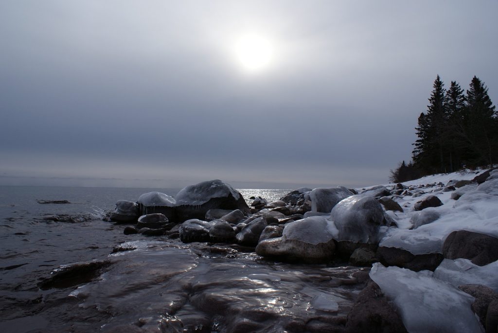 Lake Superior in the winter. Trees in the background, ice on rocks in the centre of the photo.