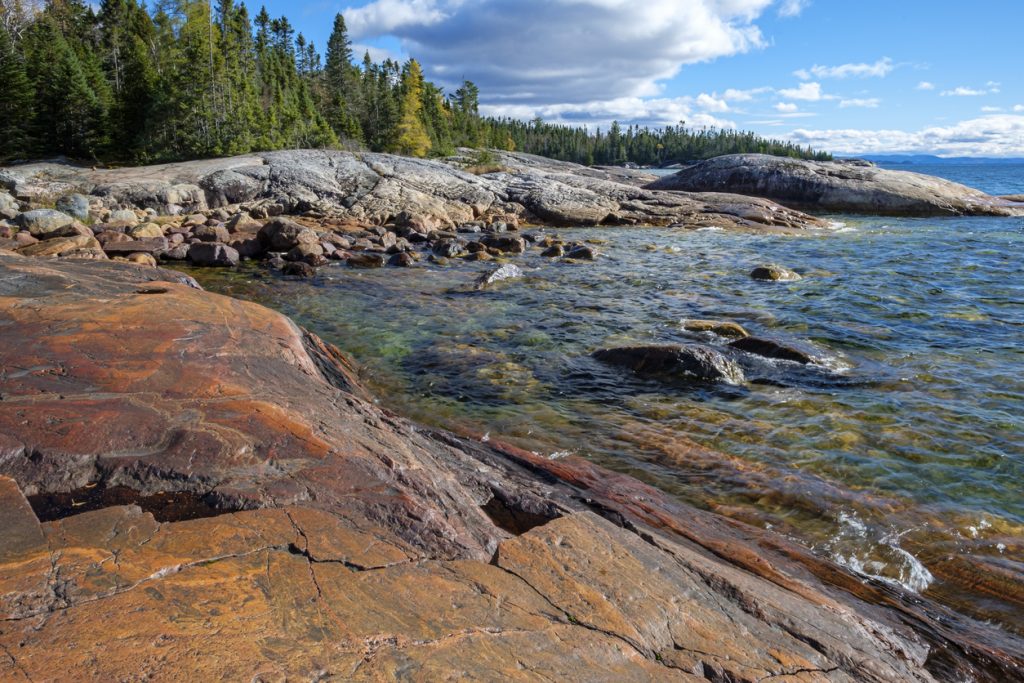 Shore of Lake Superior with rocks in the foreground and trees in the background. 